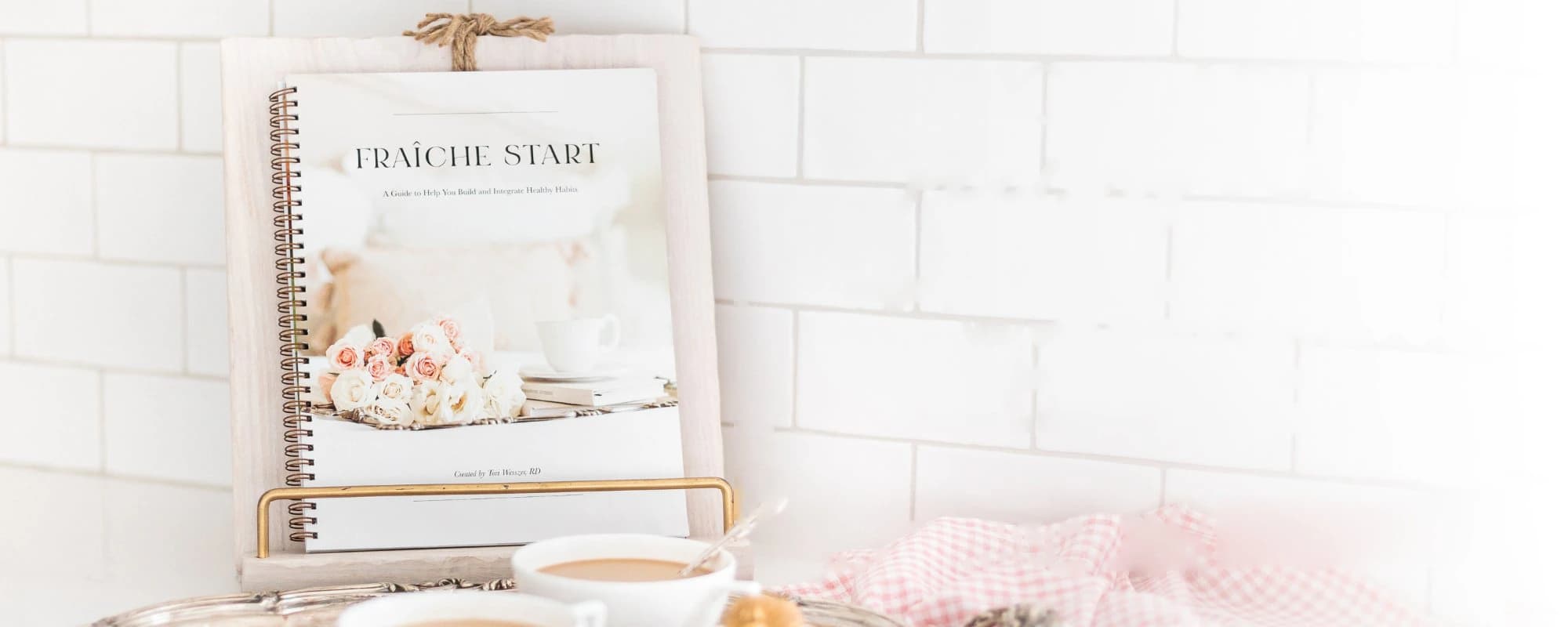 The Fraîche Start workbook on a stand beside a cup of coffee