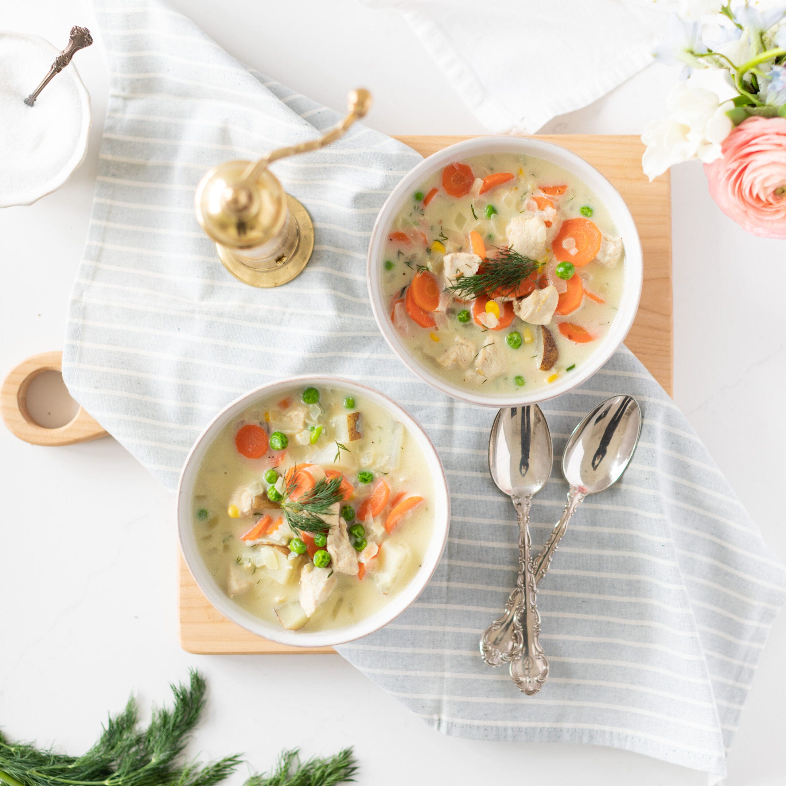 two bowls of gluten free chicken chowder topped with fresh dill and carrots and peas