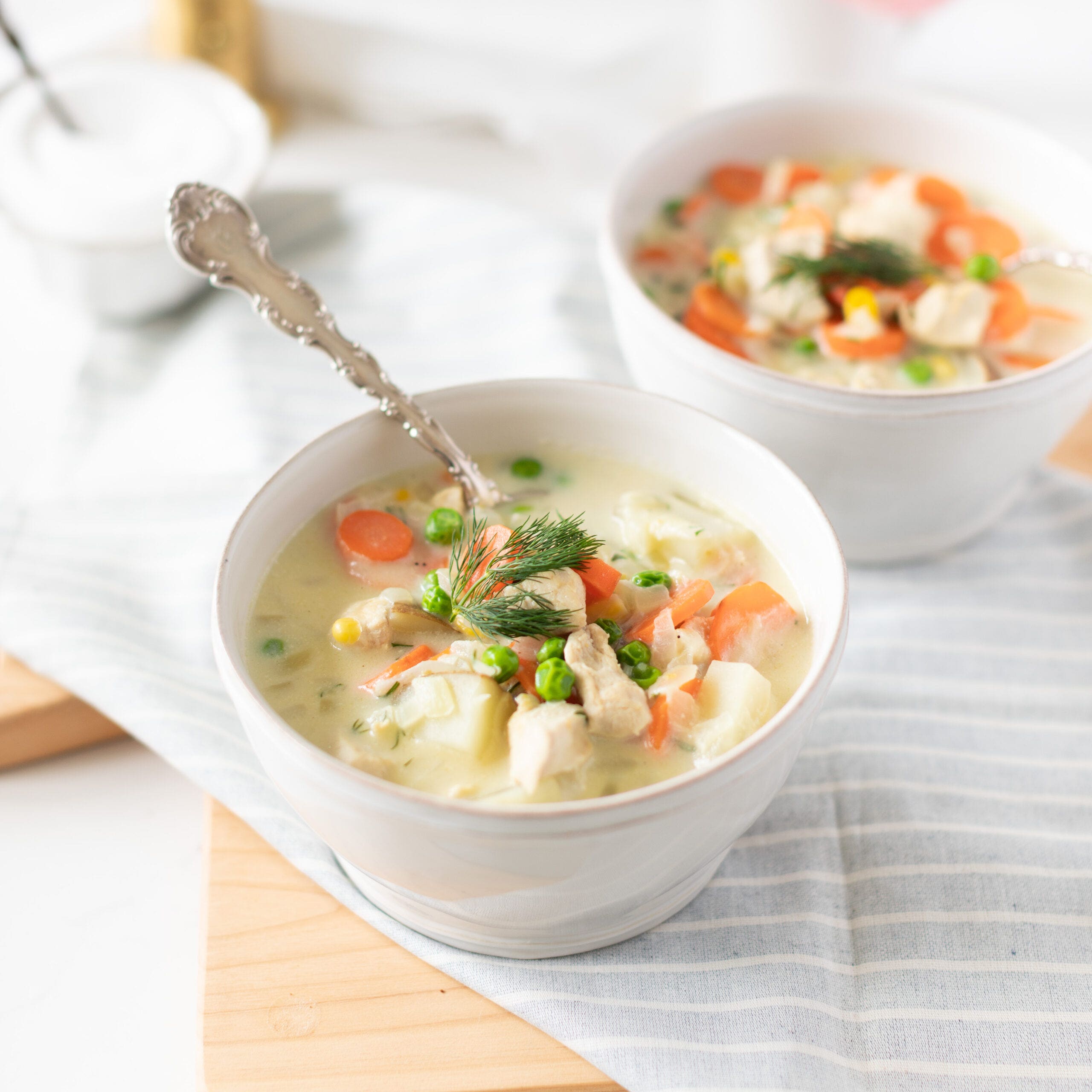 two bowls of chicken chowder with peas, carrots, and potato topped with dill