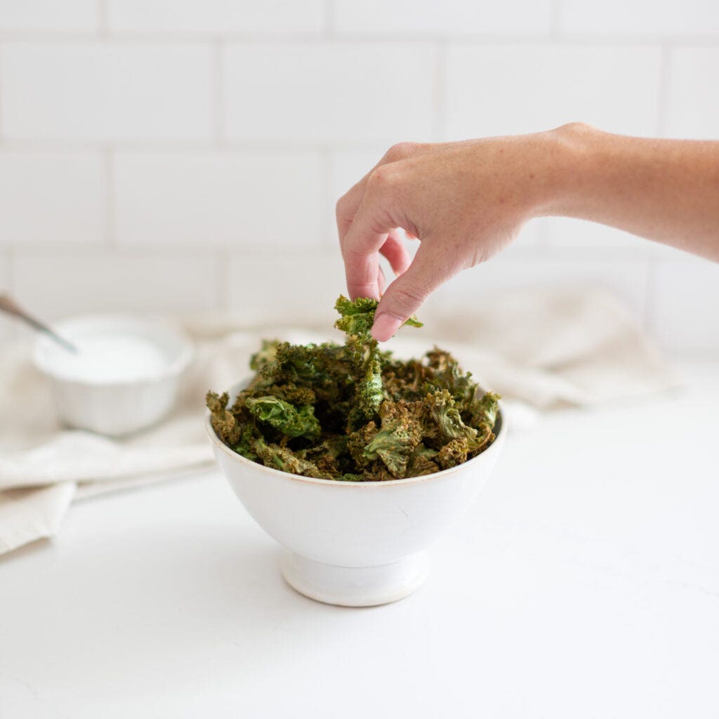 a hand grabbing kale chips from a small bowl