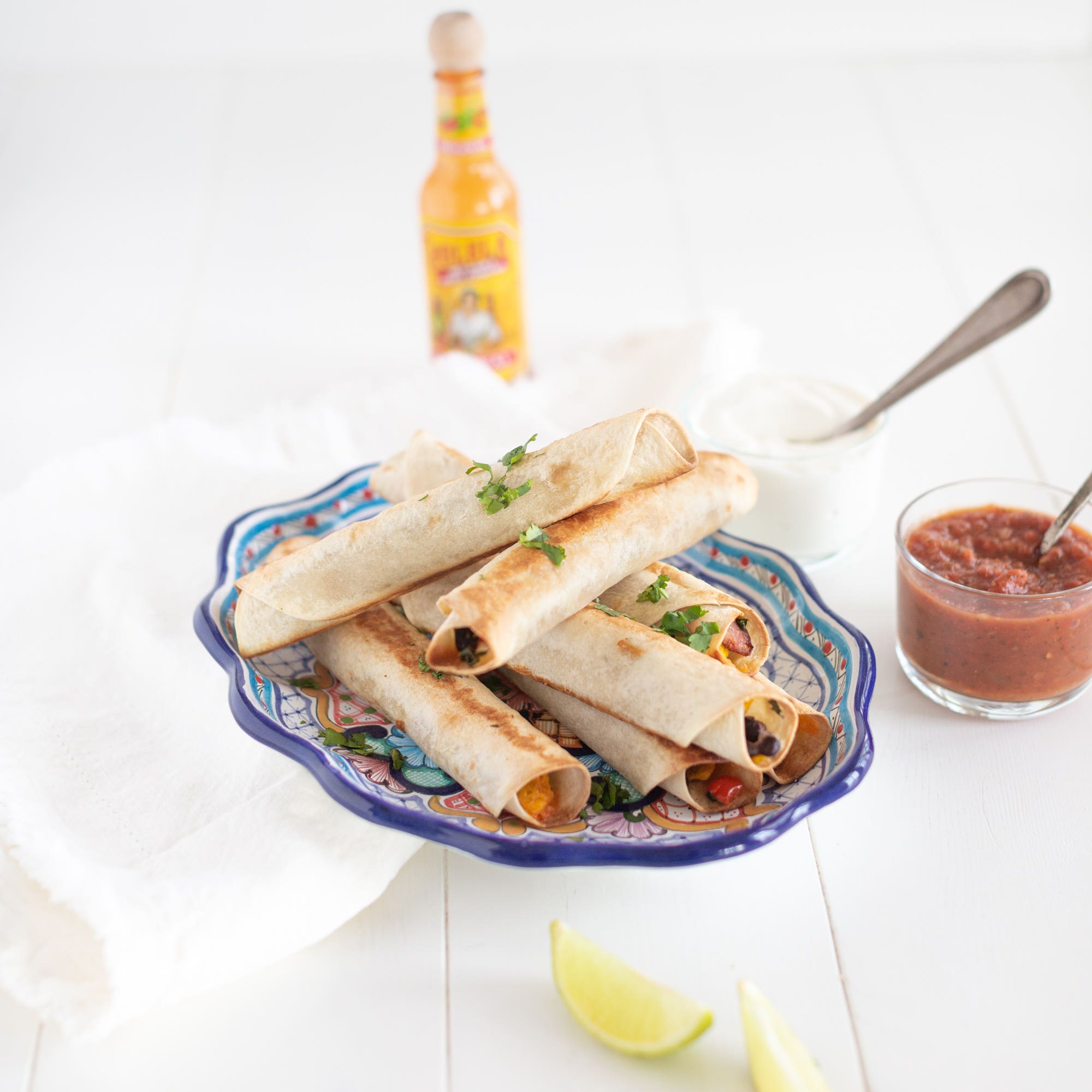 breakfast taquitos plated with salsa, lime and hot sauce