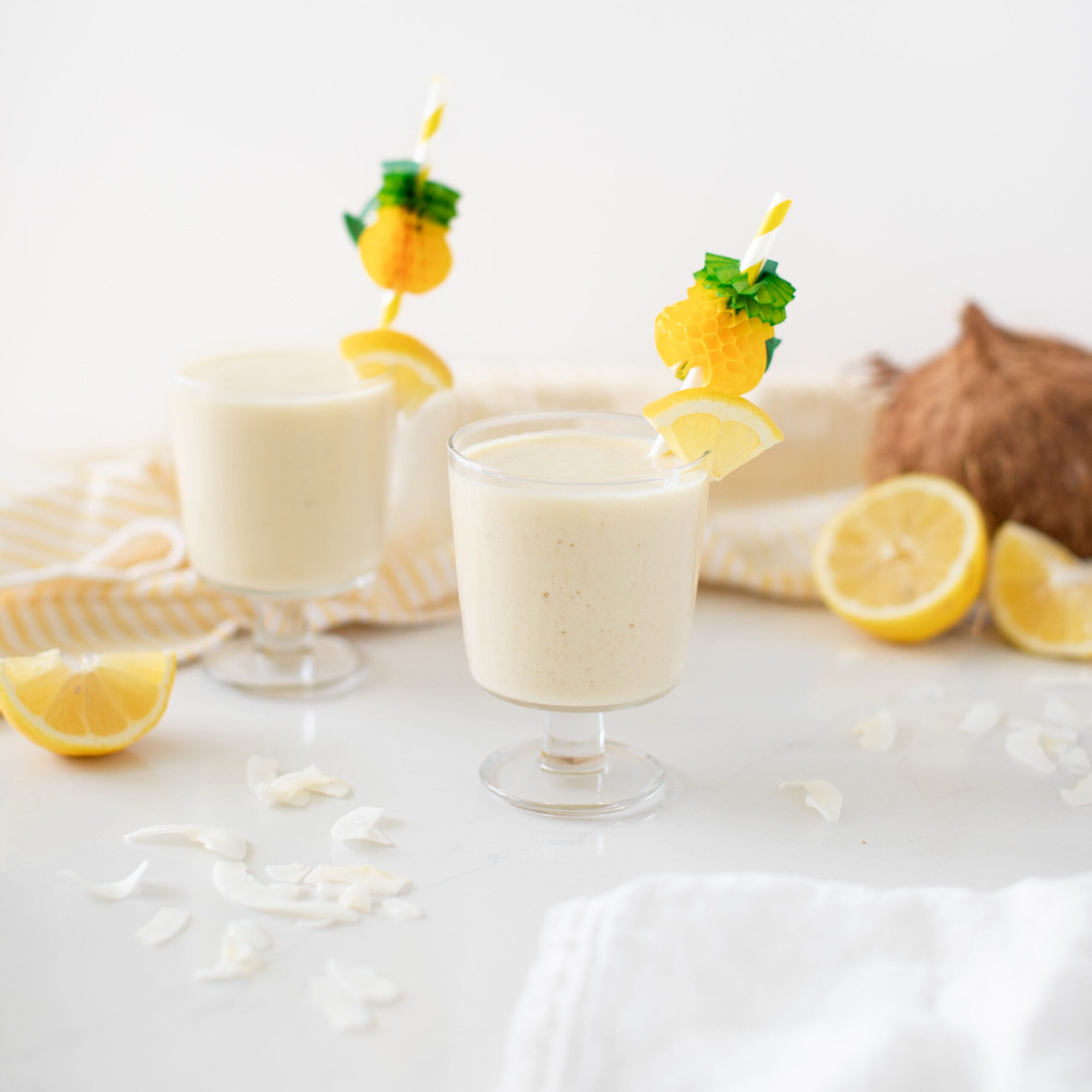 two coconut lemonade smoothies surrounded by lemons and coconut