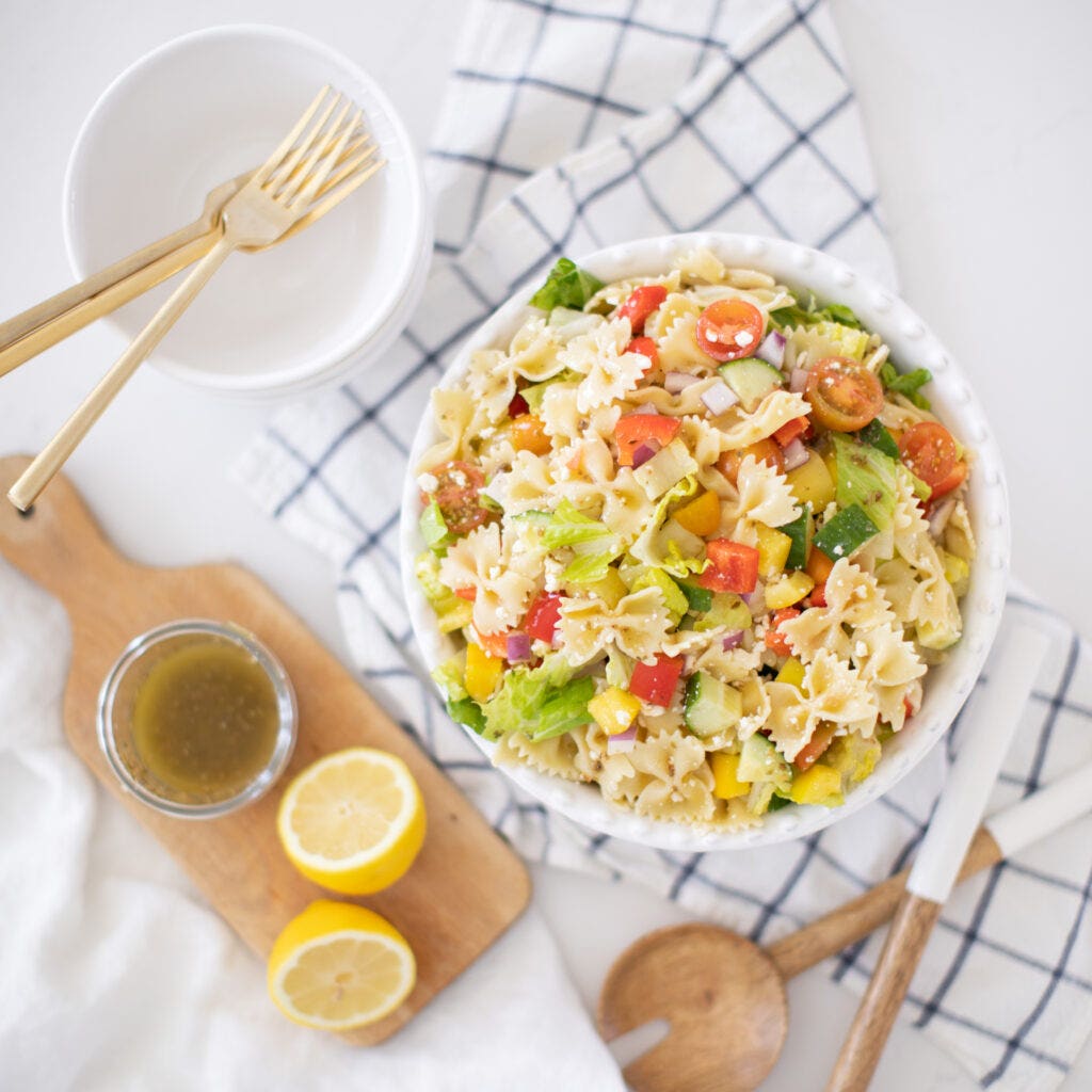 A large bowl of Greek Pasta Salad including bow tie pasta, tomato, lettuce, peppers, cucumber, red onion, feta, and homemade greek dressing. This meal is perfect for a summer getaway.