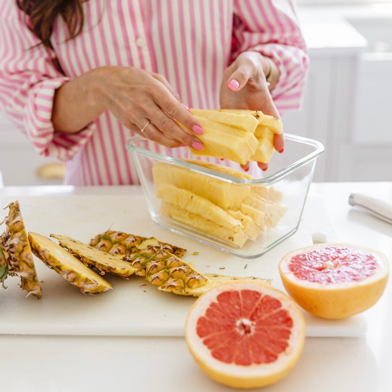 Women packing cut up pineapple as a snack in glass meal prep containers.