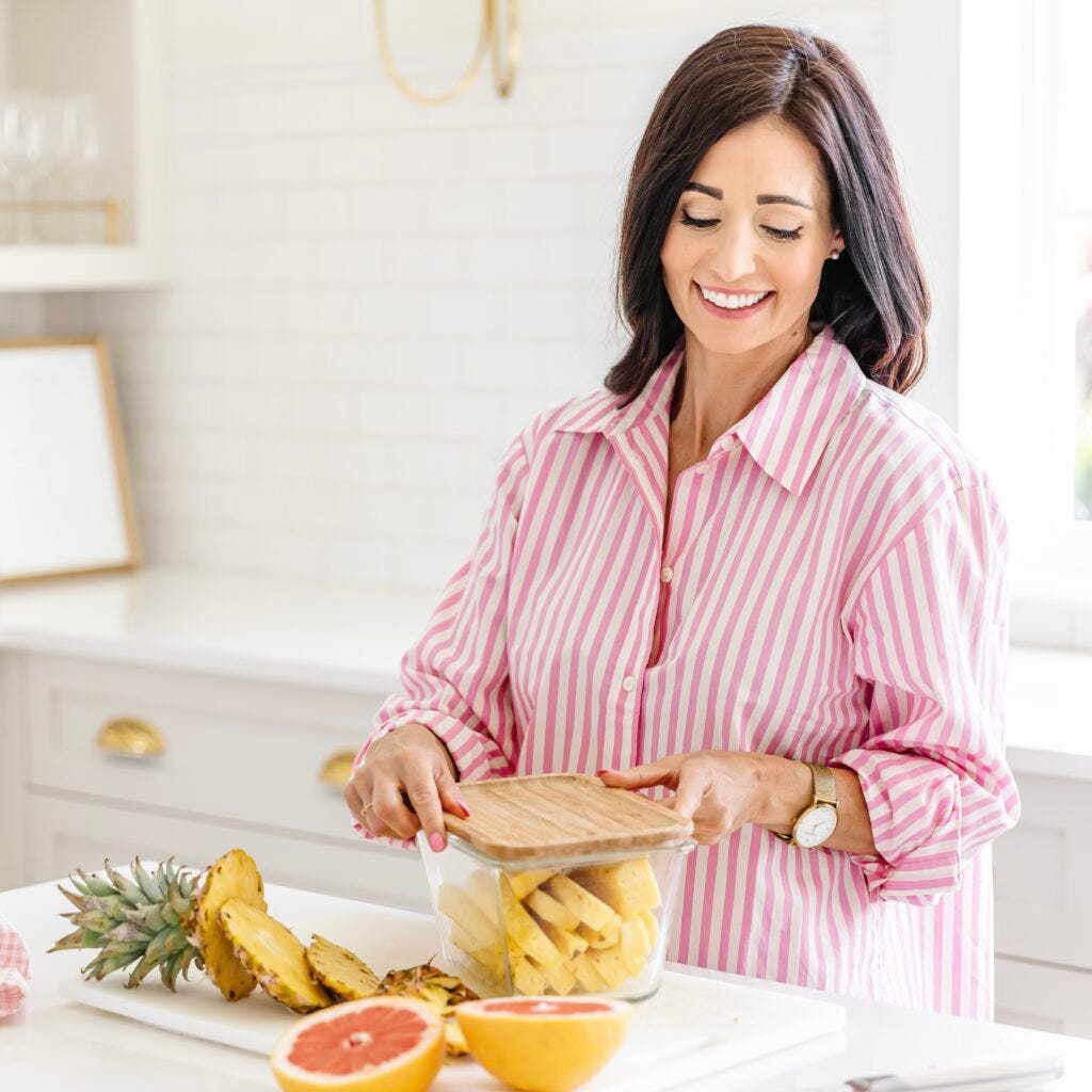 Women putting cut up pineapple in a class container to take as a kid-friendly road trip snack. 