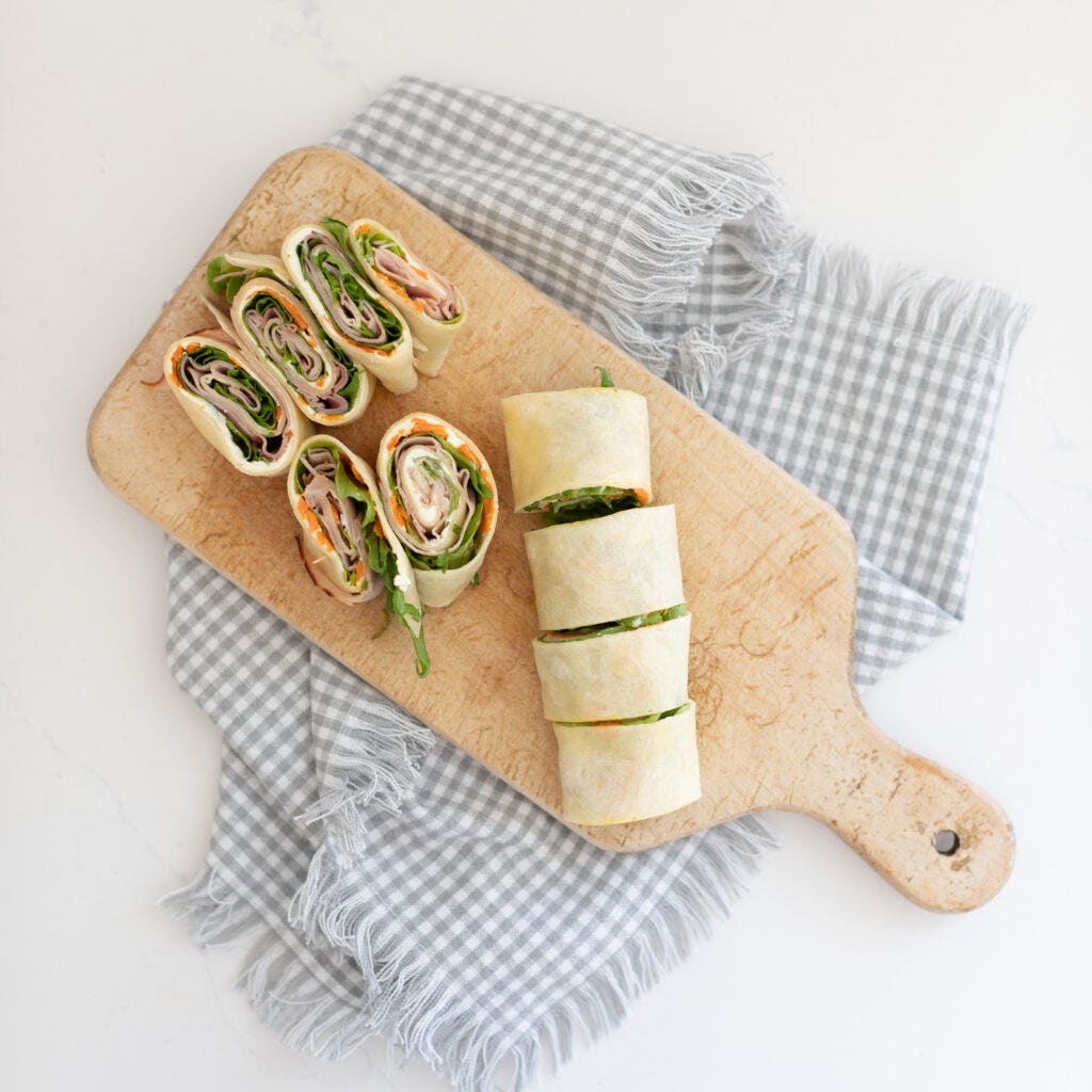 A wrap filled with cream cheese, carrots, lettuce, and deli turkey, which is then rolled up and sliced to make hand help Turkey Pinwheels.