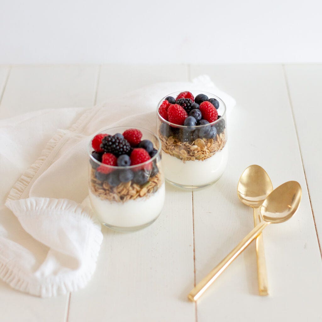 Two class cups filled with greek yogurt, homemade granola and berries to make berry yogurt parfaits. 