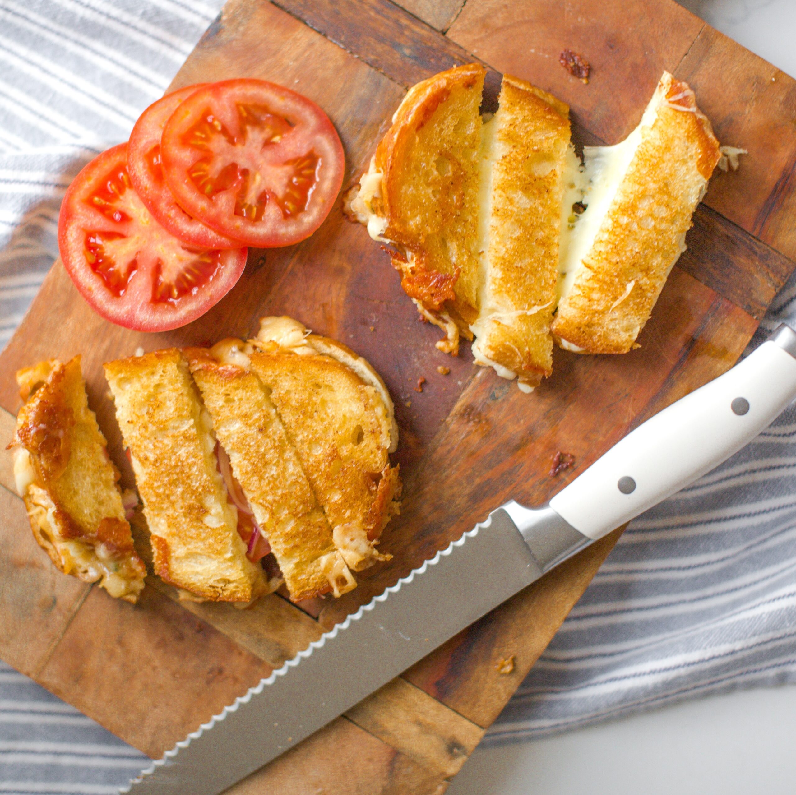 sliced grilled cheese sandwiches on a cutting board with slices of tomato beside