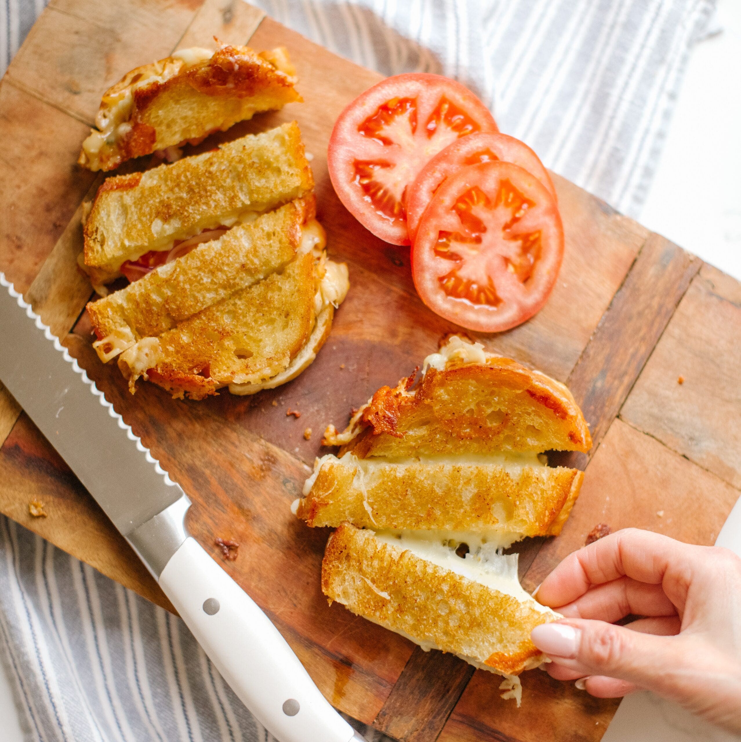 sliced grilled cheese sandwiches on a cutting board with slices of tomato beside