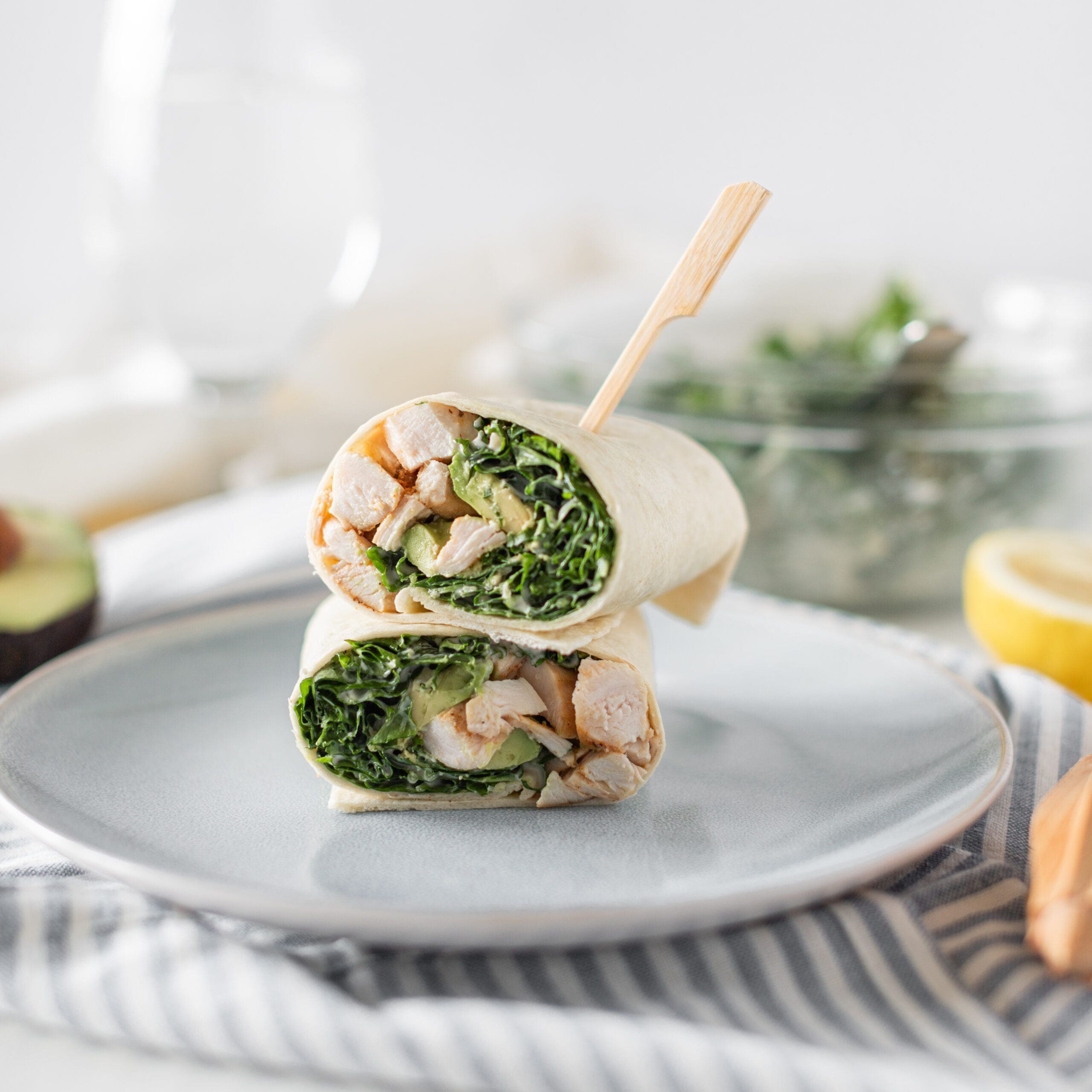 Tortilla wrap cut in half on a plate showing kale chicken and avocado inside