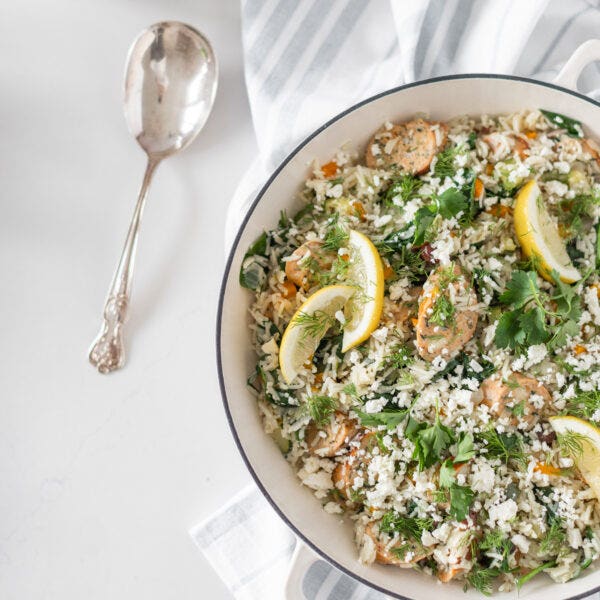 white pan with a rice and sausage dish with fresh herbs, feta cheese and lemon slices on top.