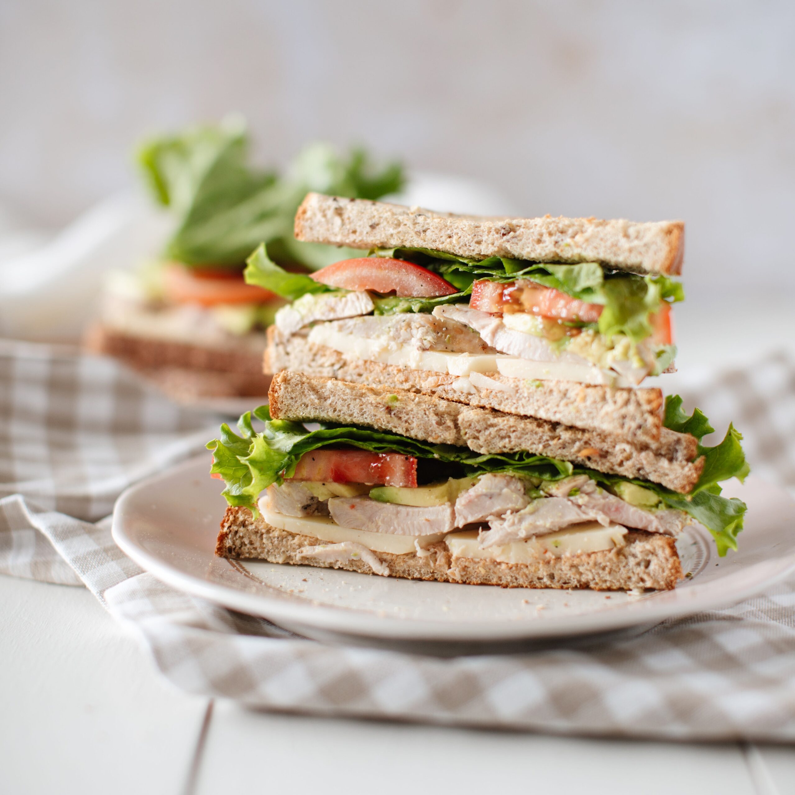 sandwich halves stacked on each other on the plate with chicken, avocado, cheese, lettuce and tomato