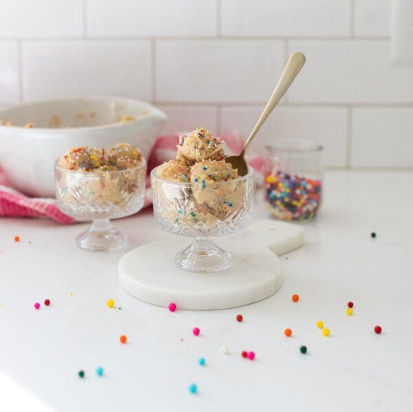 small scoops of edible cookie dough an a glass serving dish, with a dish of rainbow colour sprinkles behind