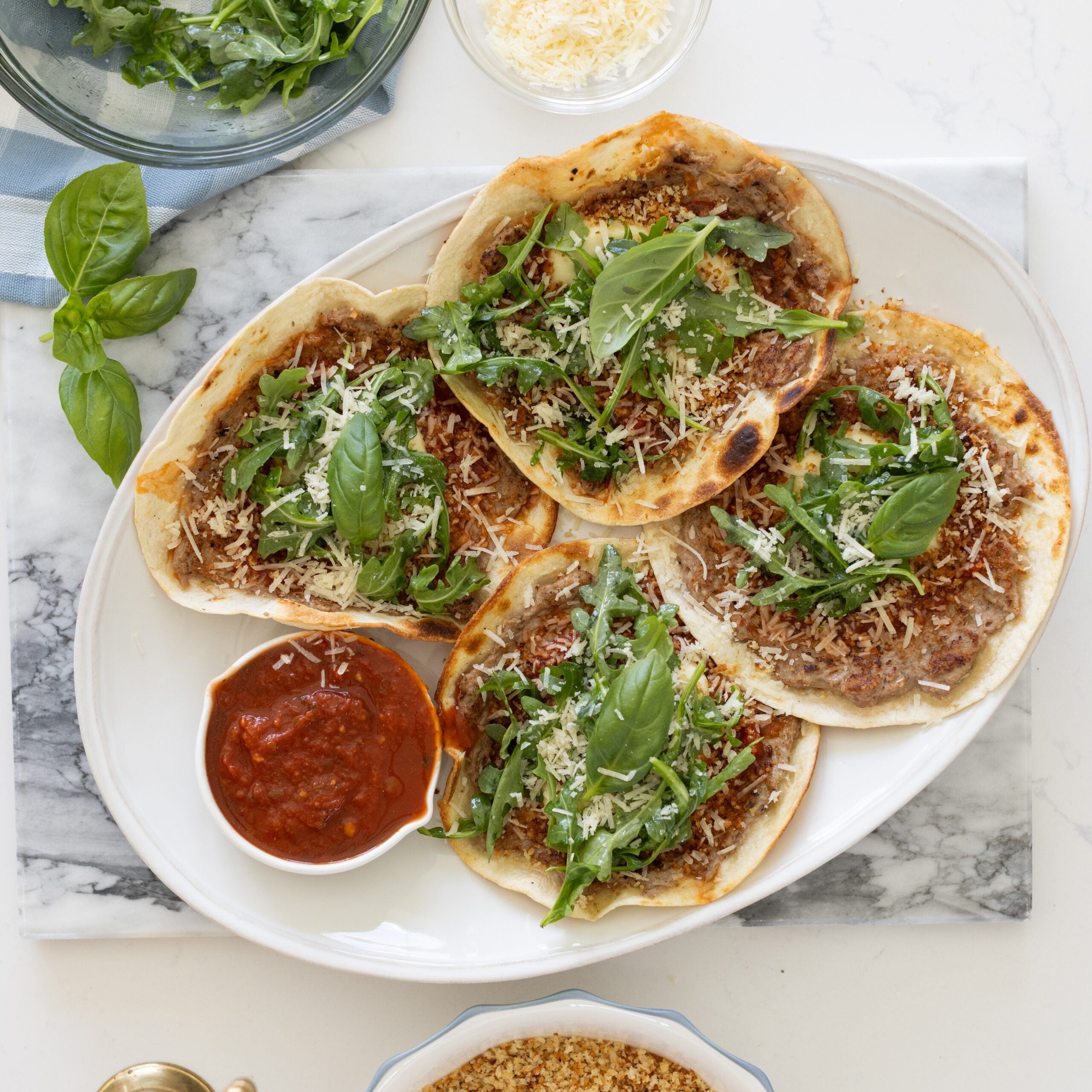 4 tacos topped with arugula on a white place with a side dish of marinara