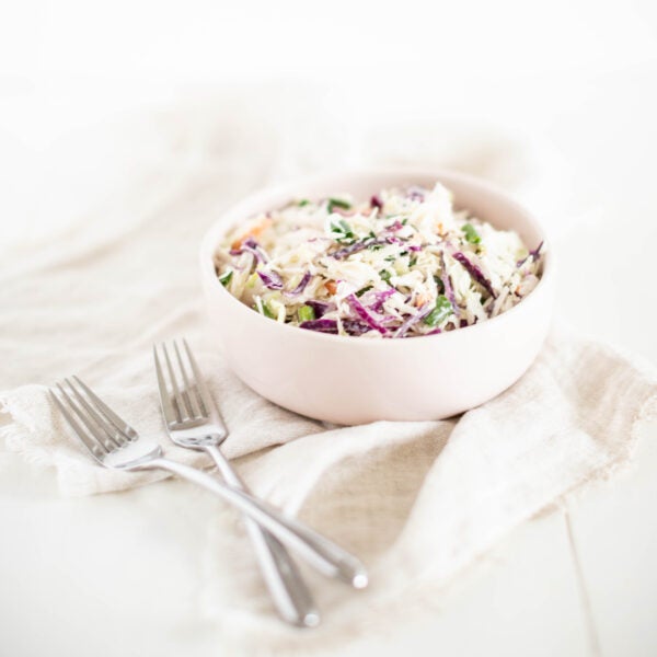 coleslaw in a white bowl with two forks beside it