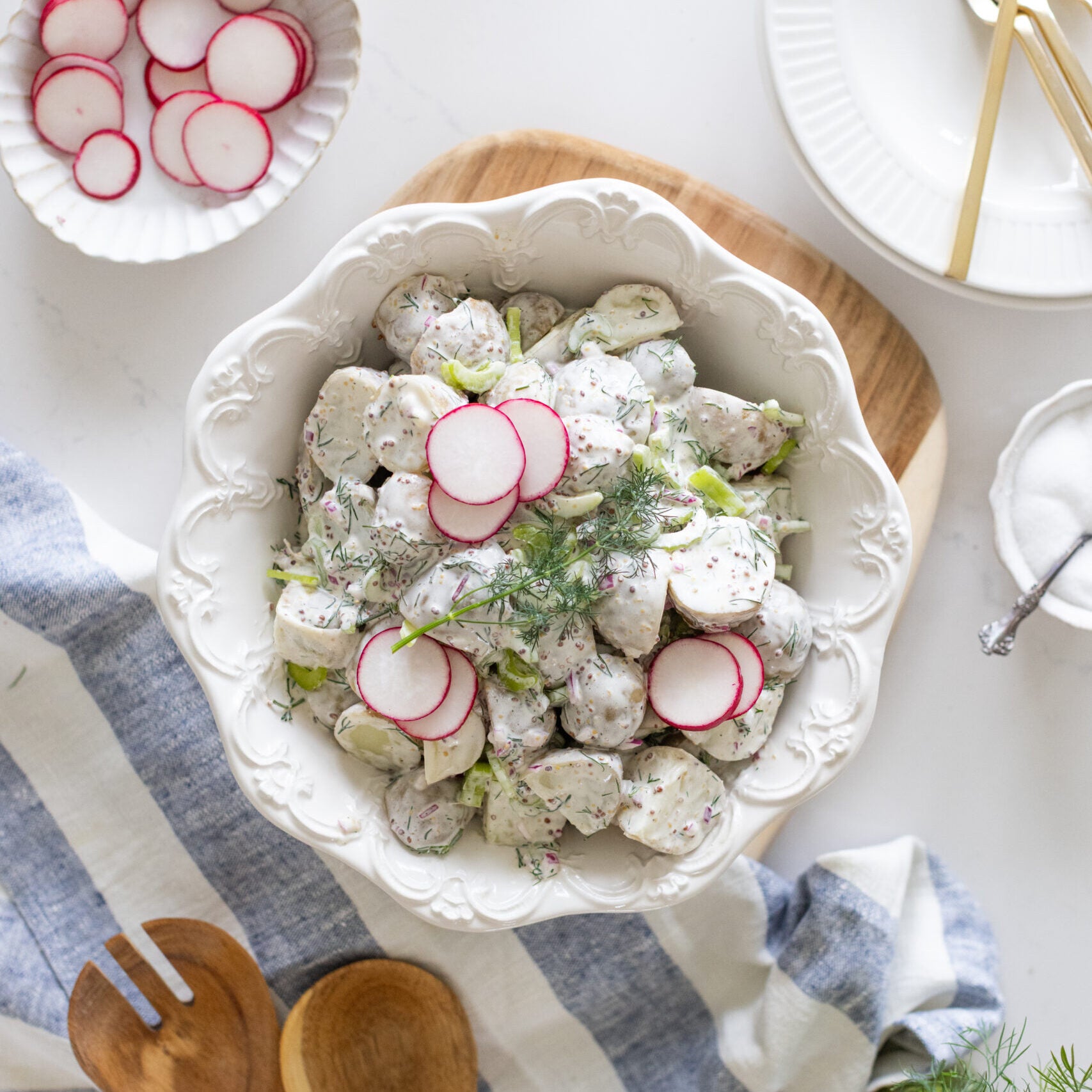 white bowl filled with potato salad garnished with sliced radishes and dill