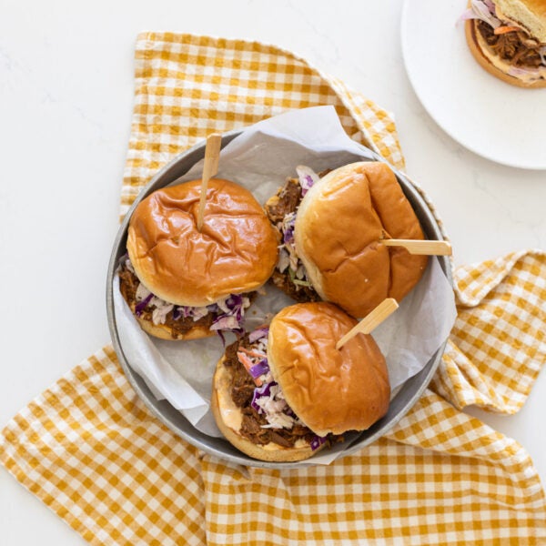 three pulled pork sandwiches on a plate with checkered yellow napkin in the background
